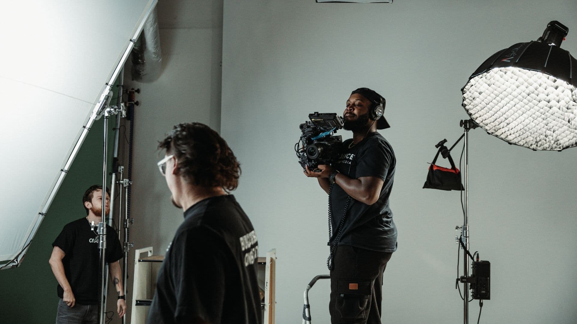 Camera operator filming talent against a grey seamless cyclorama with a softbox overhead
