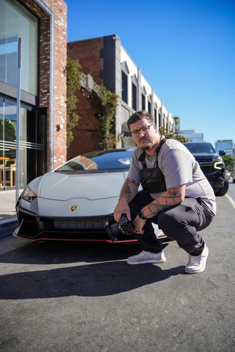 Talent crouched beside an orange Lamborghini Huracan outside a brick building in West Hollywood