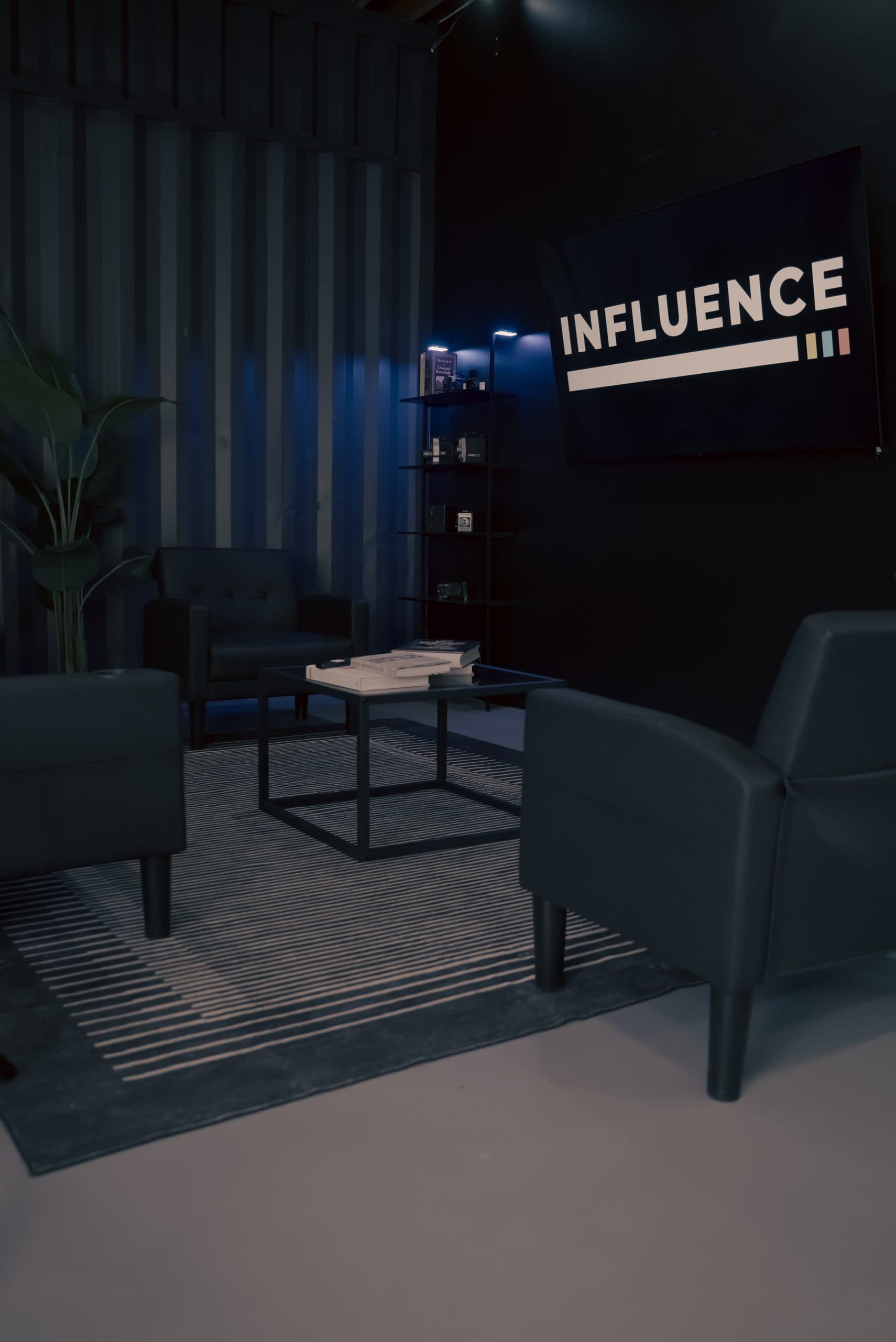 Blue-lit studio lounge set with a back-lit INFLUENCE sign on the wall